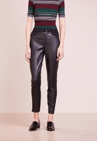 Svarta läderbyxor med en slank, åtsittande design, med framfickor och en mjuk yta. Bärs med en randig, åtsittande topp och svarta skor.