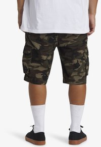 Cargo shorts in camouflagepatroon, gemaakt van katoen, hebben zijzakken en zijn gecombineerd met zwarte sneakers en witte crew socks.