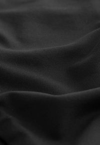 Črn rebrast material z gladko, rahlo sijočo površino, ki prikazuje subtilne valovite vzorce in gube.