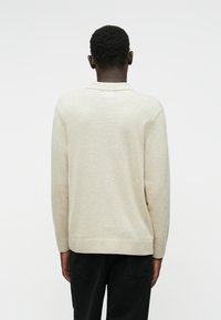 Μπεζ πλεκτό πουλόβερ με γιακά, μακριά μανίκια και ίσιο στρίφωμα, με λεία υφή και ελάχιστες σχεδιαστικές λεπτομέρειες.