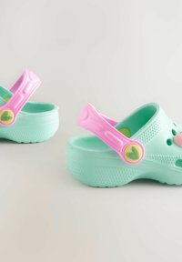 Zuecos de un suave verde menta con correas rosas, decoraciones en forma de corazón, orificios de ventilación y suelas texturizadas para mayor agarre y comodidad.