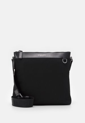 Sac bandoulière noir Michael Kors avec sangle ajustable et fermeture éclair sur le dessus, avec des éléments métalliques argentés et un logo sur le devant en haut.