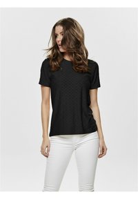 Black short-sleeve shirt with eyelet design, round neckline, and soft texture, paired with white fitted pants.