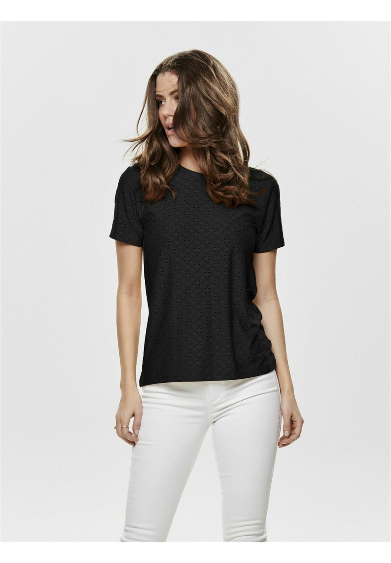 Black short-sleeve shirt with eyelet design, round neckline, and soft texture, paired with white fitted pants.