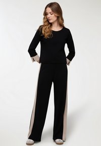 Maglietta nera a maniche lunghe con dettagli beige e pantaloni neri abbinati caratterizzati da strisce laterali beige. Tessuto morbido con una vestibilità comoda.