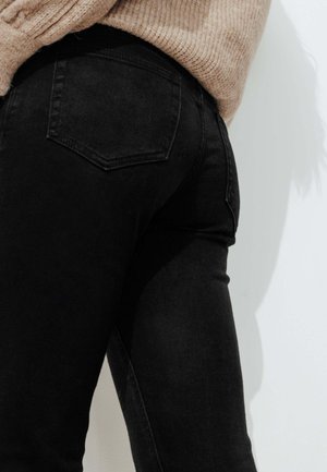 Jean noir en denim avec une coupe ajustée, une taille mi-haute, un style à cinq poches et des coutures discrètes sur les poches arrière.