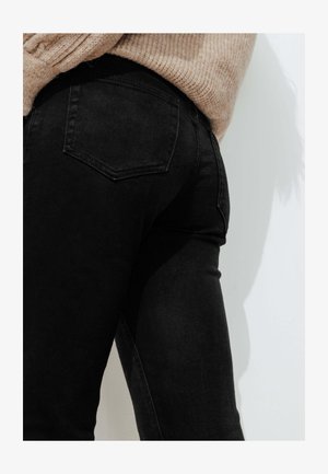 Jean noir en denim avec une coupe ajustée, une taille mi-haute, un style à cinq poches et des coutures discrètes sur les poches arrière.