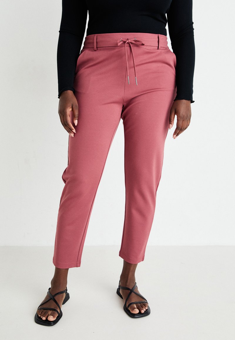 Rose-colored trousers with a relaxed fit, drawstring waist, smooth texture, and tapered design. Paired with black strappy sandals.