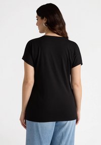 Czarny t-shirt o luźnym kroju, z krótkimi rękawami i okrągłym dekoltem. Gładka tekstura, noszony z jasnoniebieskimi spodniami w szerokim kroju.