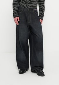 Μαύρο τζιν παντελόνι με φαρδιά μπατζάκια και ψηλή μέση, με χρυσές ραφές, εμπρόσθιες τσέπες και ετικέτα με το λογότυπο στη μέση.