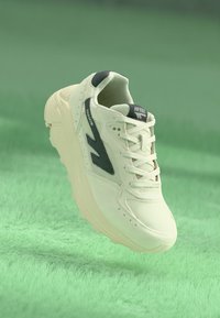 White athletic shoe with mesh and suede material, featuring black accents and a prominent logo. Chunky sole and lace-up design.