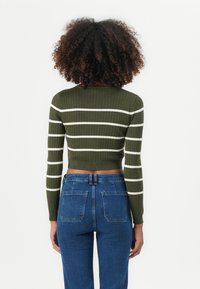 Oliven grønn ribbestrikket crop-genser med hvite horisontale striper, med lange ermer og en tettsittende design, kombinert med blå denimjeans.