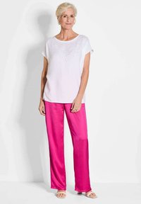 Witte blouse met korte mouwen en glinsterende details bij de halslijn, gecombineerd met felroze satijnen broeken en beige sandalen.