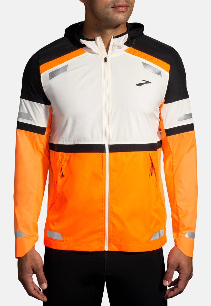 Veste de course en tissu léger, avec un corps blanc, des manches noires et des accents orange. Comprend des réflecteurs et des poches zippées.