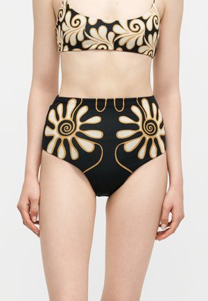 Kobieta nosząca czarne bikini z wysokim stanem oraz górę z beżowymi i złotymi abstrakcyjnymi kwiatowymi wzorami.