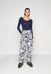 Tengerészkék hosszú ujjú felső fehér nadrággal, amely absztrakt fekete mintázattal rendelkezik. A modellen díszes hardverrel ellátott fekete cipők vannak.