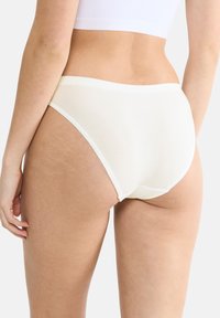 Kremowe bawełniane majtki o gładkiej teksturze, wysokim stanem oraz kontrastowym wykończeniu z elastycznego materiału wzdłuż pasa i otworów na nogi.