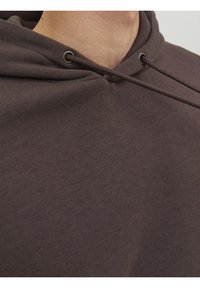 Gros plan d'une personne portant un sweat à capuche marron foncé avec des cordons attachés près du cou.