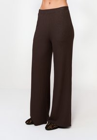 Hnedé rebrované nohavice s širokými nohavicami a vysokým pásom, vyrobené z jemného materiálu. Majú voľný strih, ktorý sa smerom k lemom rozširuje.