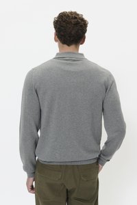 Felpa grigia con colletto, maniche lunghe e polsini a costine, abbinata a pantaloni verde oliva con tasche posteriori.