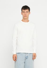 Camicia bianca in cotone a maniche lunghe con colletto tondo, abbinata a pantaloni corti in denim azzurro. Tessuto morbido, design semplice, stile minimalista.
