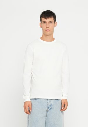 Pikkade varrukatega valge puuvillane särk ümmarguse kaelusega, koos helesiniste teksashortsidega. Sile tekstuur, põhikujundus, minimalistlik stiil.
