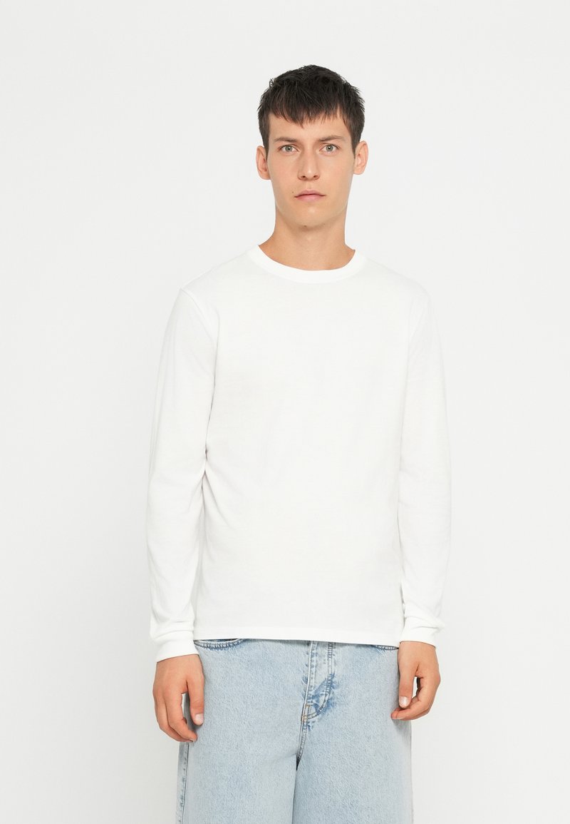 Camicia bianca in cotone a maniche lunghe con colletto tondo, abbinata a pantaloni corti in denim azzurro. Tessuto morbido, design semplice, stile minimalista.