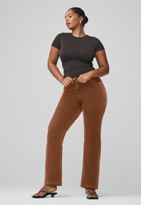 Pantalones de pana marrón acampanados con un acabado texturizado, combinados con una blusa negra de manga corta ajustada y sandalias negras.