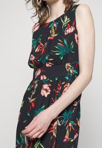 Schwarzes Kleid mit bunten Blumenmustern, ärmellosem Design, gerafftem Bund und fließendem Stoff. Auffällige lebendige Farben sind rot und grün.