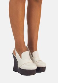 Sandali wedge bianchi con suola spessa in sughero, caratterizzati da un ampia fascia sulla parte anteriore e un design con tacco aperto. Materiale in pelle liscia.