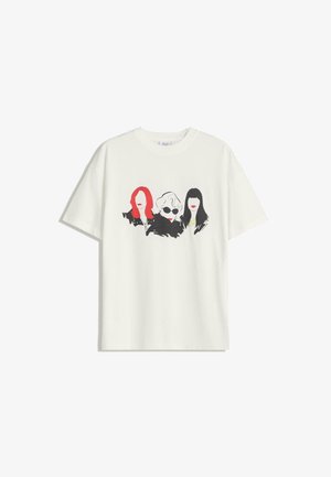 T-shirt en coton blanc avec un motif de trois femmes aux cheveux rouges et noirs, lunettes de soleil et lèvres rouges vives, sur un fond uni.