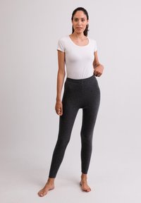 Grijze, aansluitende legging met een elastische tailleband, gemaakt van een zachte, gestructureerde stof; gecombineerd met een eenvoudig wit t-shirt met korte mouwen.