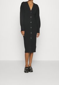 Robe cardigan noire avec encolure en V, manches longues et fermeture à boutons sur le devant. Présente une silhouette ajustée, une longueur jusqu'au genou et une texture côtelée.