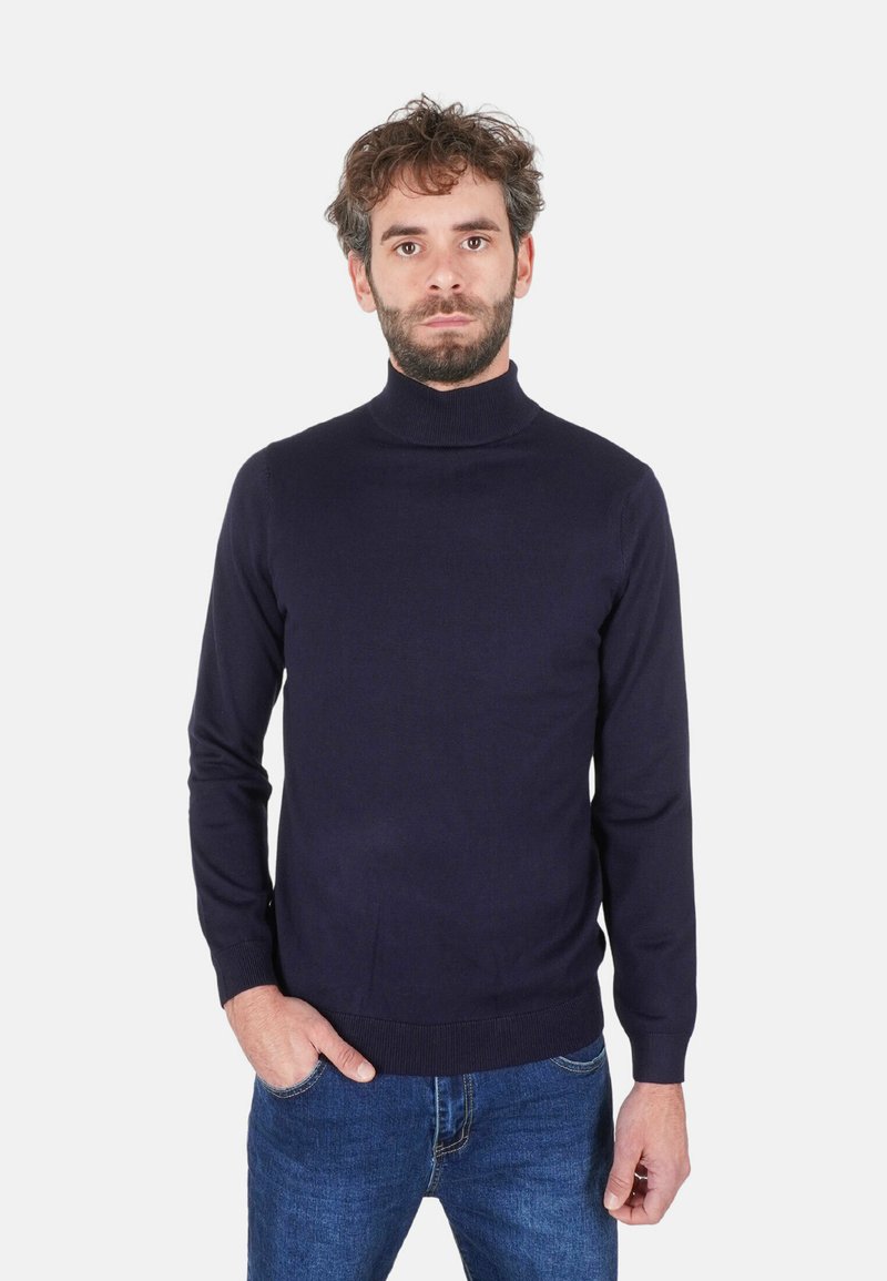 Maglione dolcevita blu navy realizzato in tessuto liscio, con design aderente e polsini a coste, indossato con jeans blu.