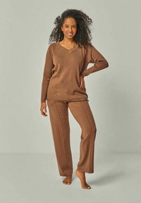 Braunes Strick-Loungewear-Set mit einem langärmligen V-Ausschnitt-Oberteil und passenden Dralon-Pants mit weit geschnittenem Bein, gefertigt aus weichem, strukturiertem Stoff mit sichtbaren Nahtdetails.