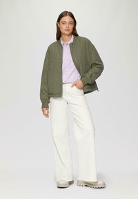 Groene bomberjack, lichtpaarse shirt, witte wijde broek en beige chunky schoenen. Eenvoudige stoftexturen met een ontspannen pasvorm.