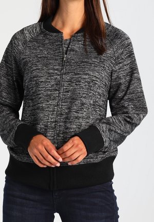 Zwart en grijs gemarmerde zipjack met een geribbelde kraag en manchetten, met een gestructureerde afwerking en een ritssluiting aan de voorkant. Gedragen met een donkere spijkerbroek.