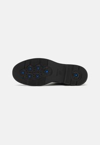 Semelle de chaussure en caoutchouc noir avec six trous de ventilation bleus, surface texturée, et un mélange de motifs lisses et striés pour l'adhérence.