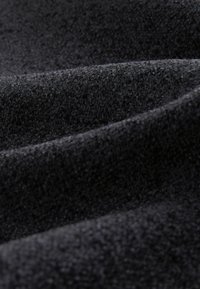 Melns audums ar mīkstu, strukturētu virsmu, kurā redzamas dažādas dziļuma un viļņu rakstu variācijas, kas liecina par mīkstu materiālu.