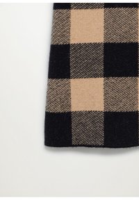 Tissu à carreaux beige et noir avec une texture en laine, montrant une section d'un vêtement sur un fond blanc uni.