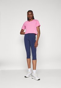Pink cropped t-shirt with a printed logo, paired with navy capri leggings featuring a floral pattern on the side. White athletic shoes.