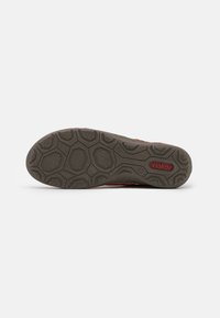 Semelle de chaussure Rieker avec une surface en caoutchouc gris texturé. Présente un motif en nid d'abeille et un logo rouge sur le côté.