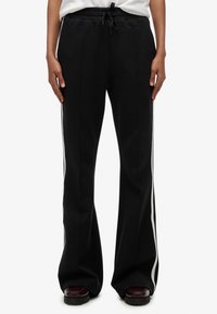 Pantalones deportivos negros con diseño acampanado, con franjas laterales blancas, cinturilla elástica y tela suave y texturizada.