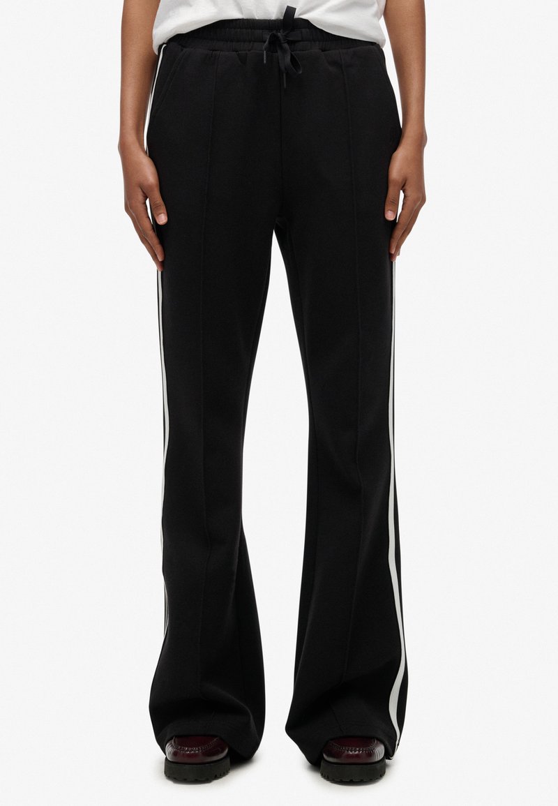 Pantalones deportivos negros con diseño acampanado, con franjas laterales blancas, cinturilla elástica y tela suave y texturizada.