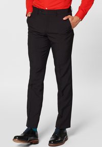 Pantaloni neri sartoriali in tessuto liscio, slim fit, con passanti per cintura, abbinati a scarpe eleganti nere e a una camicia rossa a maniche lunghe.