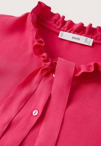 Blusa fucsia con scollo arricciato e dettaglio legato. Presenta una chiusura con bottoni e un tessuto morbido e liscio. Etichetta visibile sul retro.