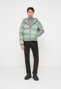Jachetă căptușită de culoare verde mentă, cu glugă, închidere cu fermoar și două buzunare. Purttă peste un pulover gri cu guler înalt, asociată cu pantaloni negri și încălțăminte neagră.