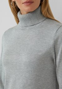 Pull à col roulé gris clair avec un col et des manches côtelés, fabriqué en tissu tricoté doux. Design texturé et ajusté.