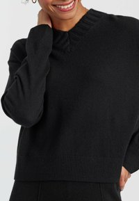 Pull en tricot noir avec un col en V et des détails côtelés au col et à l'ourlet. Texture douce, coupe décontractée et manches longues.