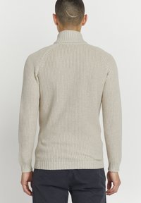 Suéter de punto beige claro con un cuello alto, dobladillo y puños acanalados, que presenta un patrón texturizado para un detalle adicional.